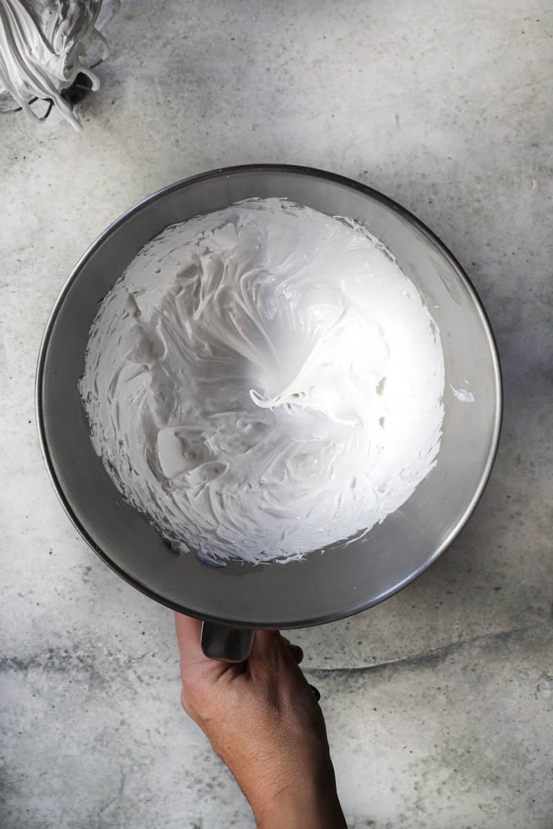 One hand holding a mixing bowl with the Swiss meringue.