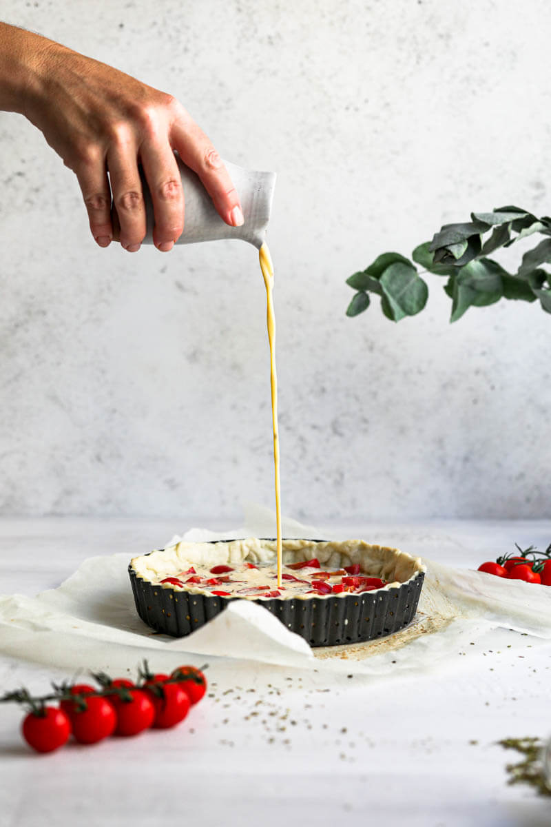 90° of the quiche batter being poured by one hand over the quiche