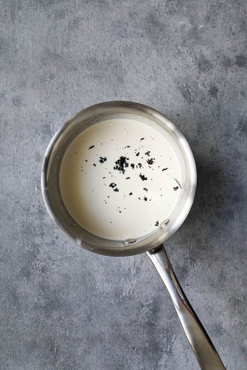 A small pan with cream and a scarped vanilla bean ready to start making vanilla bean crème brûlée.