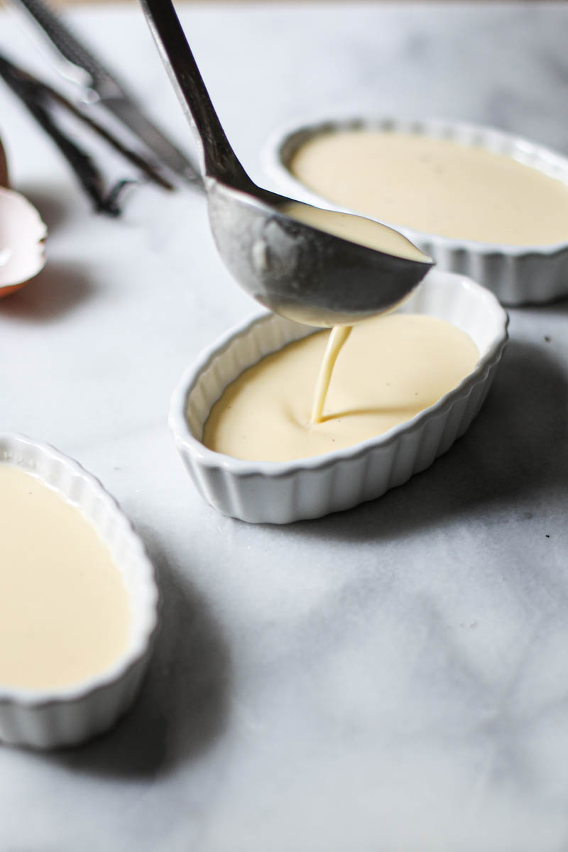 The ramekins being filled with vanilla bean crème brulee batter with a ladle.