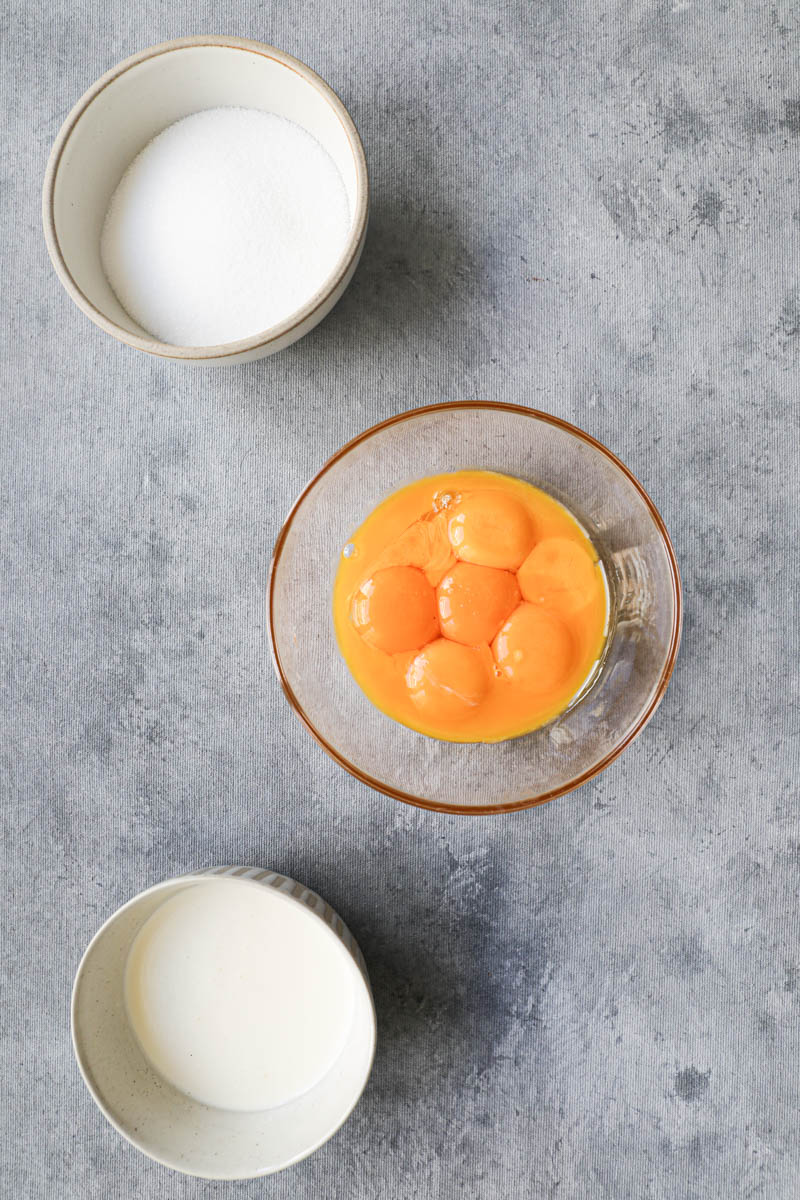 3 bowls: one with egg yolks, one with sugar and one with cream ready to start making vanilla bean crème brûlée.