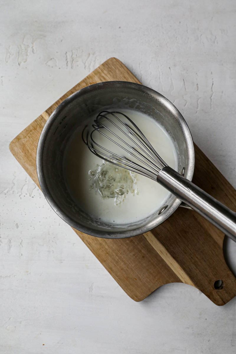 Gelatine and warm milk about to be whisked together inside a small pot.