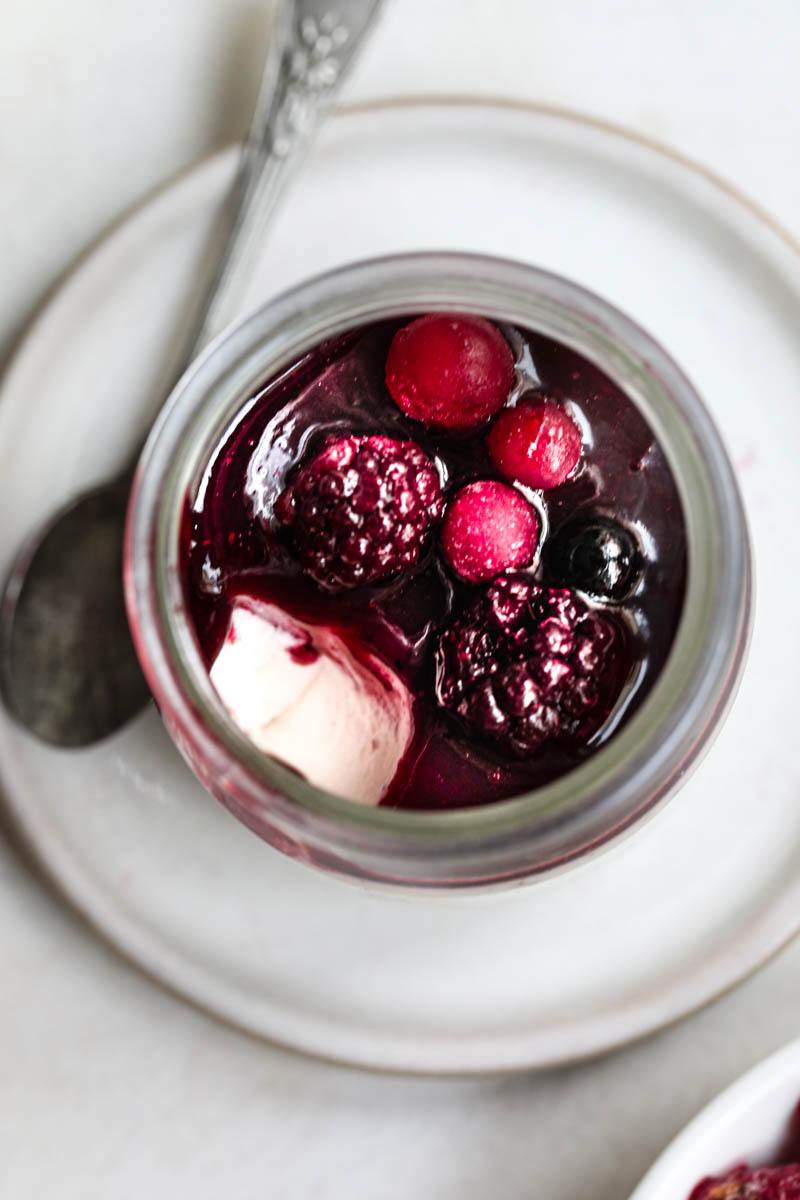 Macro shot of one small glass filled with panna cotta, berry sauce, and berries as seen from the top.