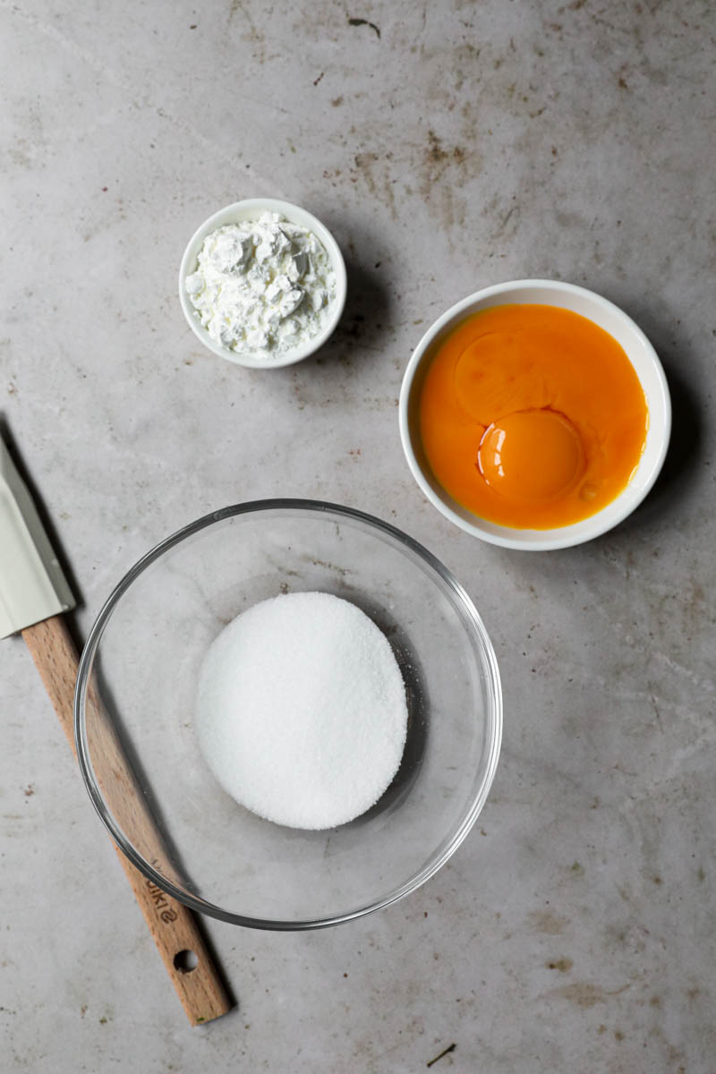 A bowl with the egg yolks, and two small bowls with sugar and cornstarch next to it.