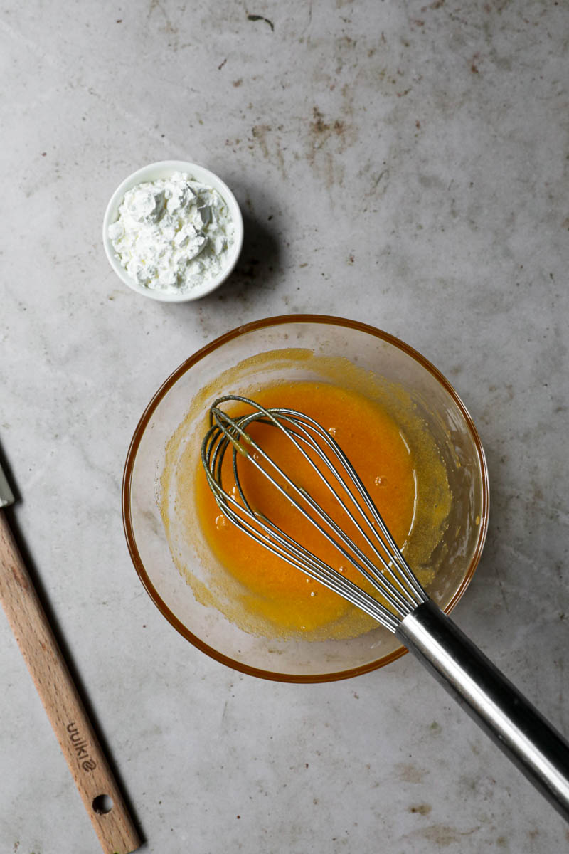 Yolks and sugar whisked together in a glass bowl with corn-starch in small bowl on the left side.