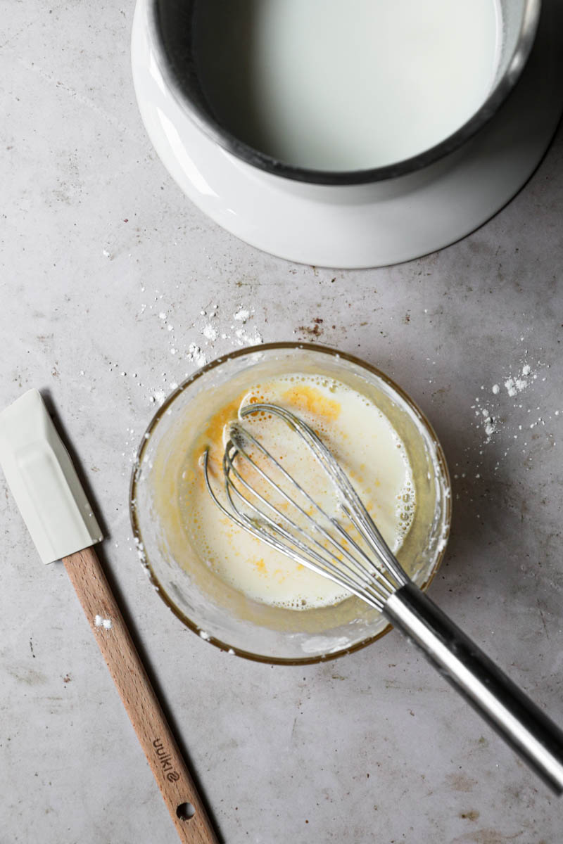 A bowl with the warm milk plus the yolk/sugar mixture with a whisk inside.