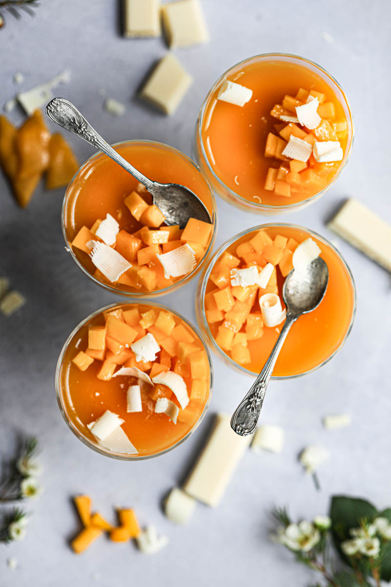 4 glasses filled with white chocolate mousse and fresh mango and mango jelly as seen from the top, with one mousse missing a bite.