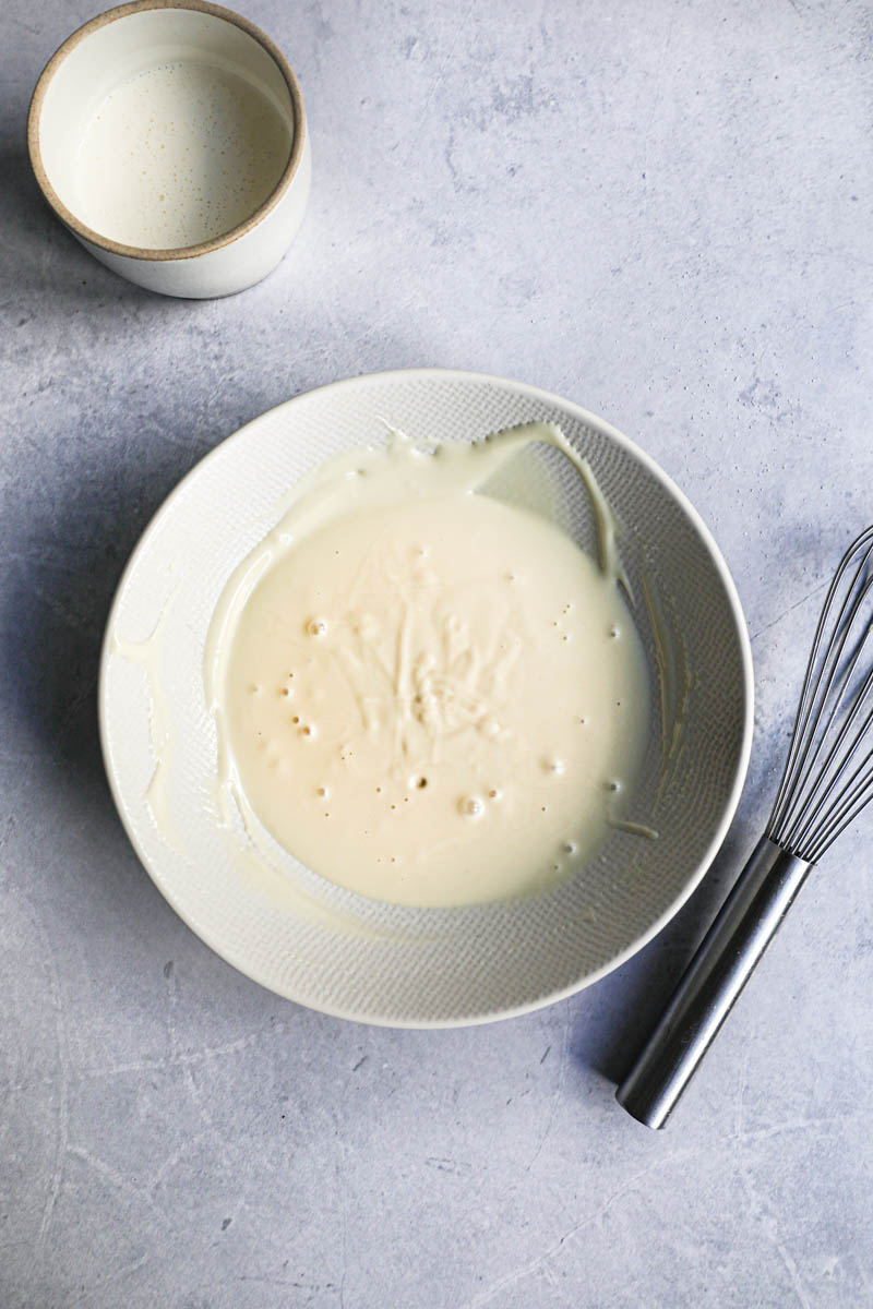 Melted white chocolate on a bowl and a small container with cream on the side.