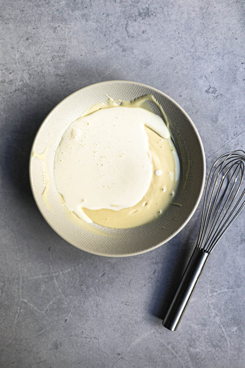 Melted white chocolate on a bowl with the cream poured over it.