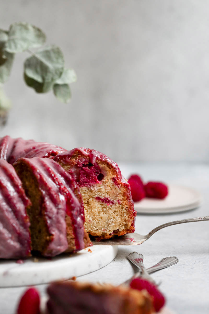 White chocolate raspberry cake seen from the side with a silver spatula pulling out one slice.