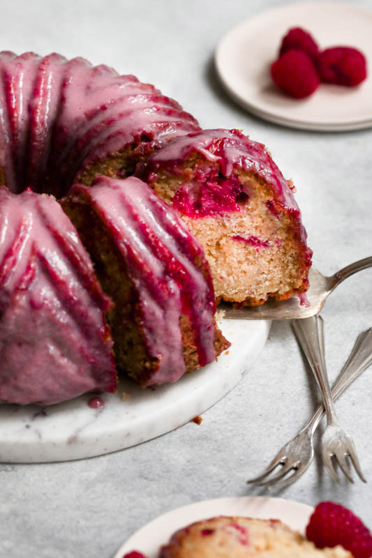 White chocolate raspberry cake seen from the side with a silver spatula pulling out one slice.