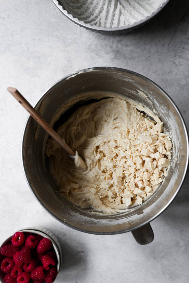 A bowl with the cake batter plus the chopped white chocolate and raspberries in a bowl on the side.