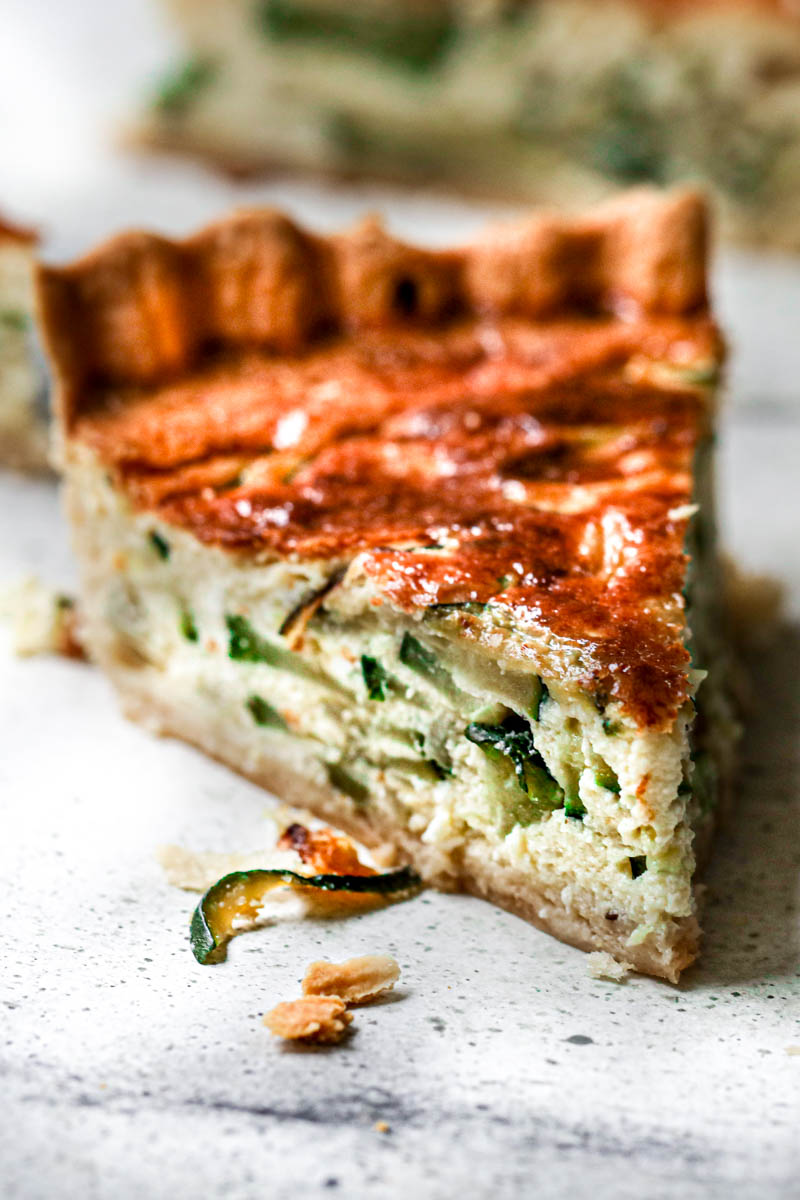 Closeup of one slice of zucchini quiche with other sliced blurry in the back.