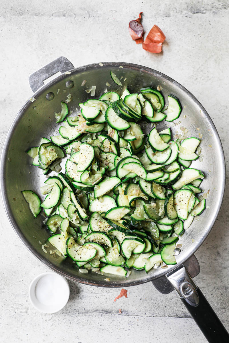 Zucchini quiche filling cooked on a pan with a and small bowl holding salt on the side.